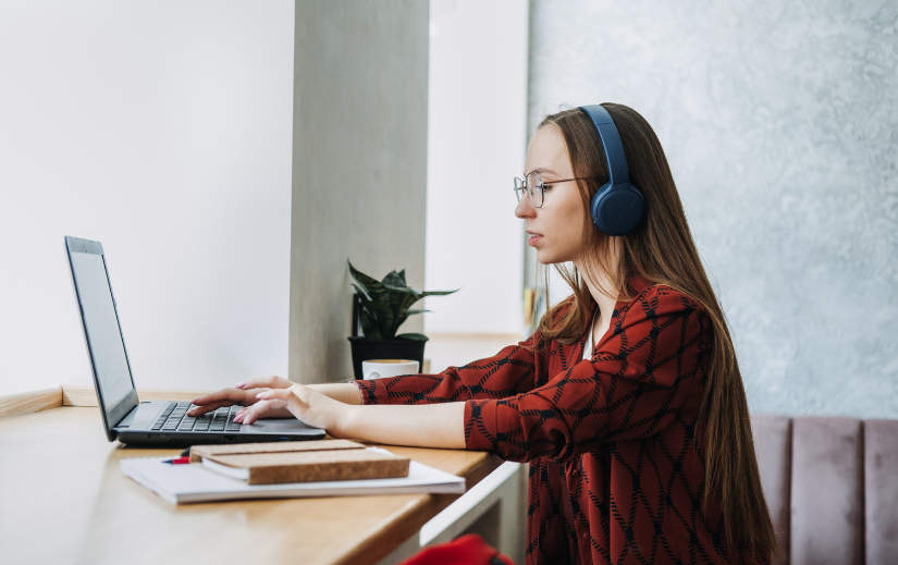 Donna che lavora al laptop con cuffie, concentrata su idee di attività secondarie per guadagnare online da uno spazio di lavoro accogliente.