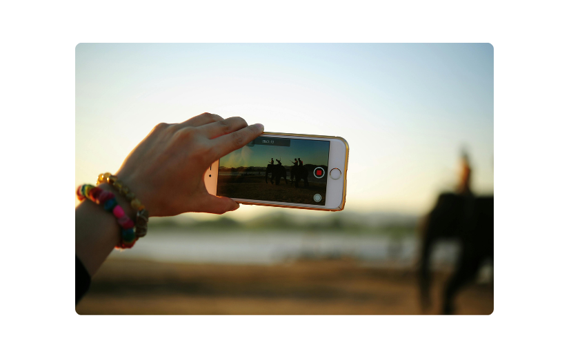 Primul plan al unei mâini care ține un smartphone care înregistrează un videoclip cu cai la apus, demonstrând crearea de conținut fără chip.