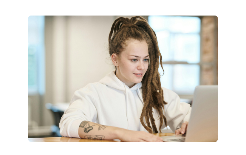 Giovane donna con una felpa bianca, al lavoro su un laptop e alla ricerca di idee creative per un reddito in uno spazio di co-working moderno.