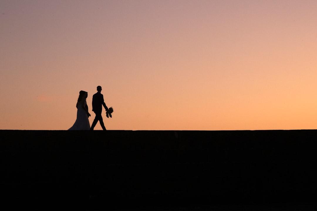 Una imagen romántica de una pareja tomados de la mano mientras caminan hacia una puesta de sol.