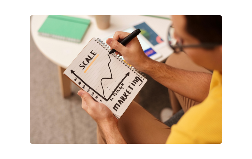 Egy marketinges egy notebookban mérleggrafikát elemez, az Amazon értékesítési trendjeit tervezi az üzleti növekedés érdekében.